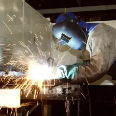 Spawacz w masce i ochronnym ubraniu pracuje przy metalowych elementach, osiągając temperaturę topnienia stali.