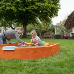 Mama i córka bawią się w piaskownicy na trawniku. Radosne zabawy w piaskownicy w słoneczny dzień.