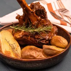 Un plat appétissant de souris d'agneau confite, tendre et savoureuse, accompagnée de pommes de terre rôties et d'une touche de romarin frais.