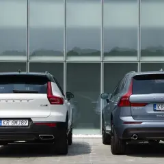 Dwa SUV-y Volvo: białe XC40 i szare XC60, stoją przed nowoczesnym budynkiem. Porównanie ich wymiarów jest łatwe.