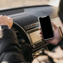 Kierowca trzyma telefon podczas jazdy, ryzykując mandat za korzystanie z telefonu.