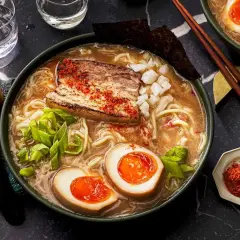 A miska pełna aromatycznego ramen co to jest? Makaron, jajko na pół, kawałek mięsa i szczypiorek w bulionie.