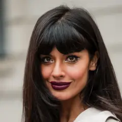 Eine Frau mit dunklen, langen Haaren und einem Pony, die einen dramatischen Lidstrich und dunklen Lippenstift trägt.