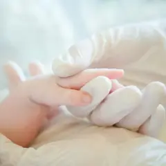 Mani guantate che tengono delicatamente un neonato, un simbolo di cura e attenzione per i possibili danni neurologici da parto.