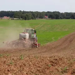 Traktor sieje, dodając do gleby niezbędne fosforany. W tle zielone pola i las.