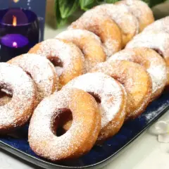 Szybkie oponki w 5 minut, posypane cukrem pudrem, wyglądają apetycznie na niebieskiej tacy. Obok świece i kwiaty.