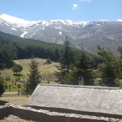 Casa rural con tejado de paja y montañas nevadas al fondo, un paisaje idílico de la fuente alta Sierra Nevada.