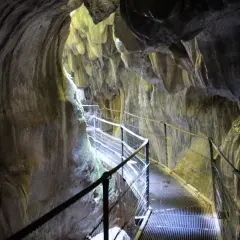 Pasarela metálica serpentea por el interior de los Gorges de la Fou, con paredes rocosas esculpidas por el agua y la luz filtrándose desde arriba.