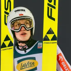 Kacper Tomasiak wzrost – młody skoczek narciarski w kasku i goglach, otoczony żółtymi nartami Fischer.