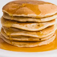 Pila di pancake proteici dorati, inzuppati di sciroppo d'acero che cola.