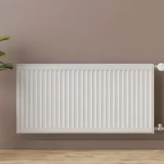 Radiador blanco de panel, un ejemplo de tipos de radiadores de agua. A su lado, una planta en maceta y una cortina.