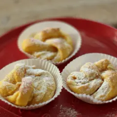 Tre saffransbullar med vit choklad, pudrade med florsocker, ligger på en röd tallrik.