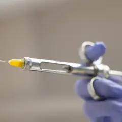 Dłoń w fioletowej rękawiczce trzyma strzykawkę dentystyczną. Co zrobić, gdy znieczulenie nie schodzi? Skonsultuj się z dentystą.