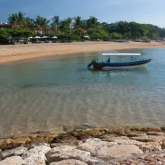 Spokojna zatoka w Sanur z łodzią "Water Walk" kołyszącą się na turkusowej wodzie. Piękna plaża z palmami i leżakami w tle.