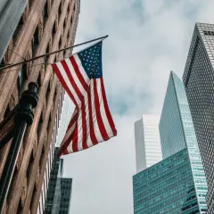 Amerykańska flaga powiewa między drapaczami chmur. Zastanawiasz się, ile kosztuje ubezpieczenie w USA?
