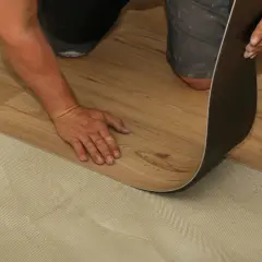 Hand verlegt Laminat auf PVC-Boden. Der Kleber ist auf dem Untergrund aufgetragen, bereit für das neue Bodenmuster.