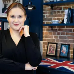 Kobieta w czarnej bluzce, otoczona brytyjskimi plakatami i książkami, idealna do kursu angielskiego C1.