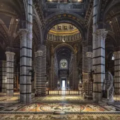 Interno del Duomo di Siena, con il suo magnifico pavimento intarsiato e le colonne a strisce bianche e nere che conducono verso l'altare.