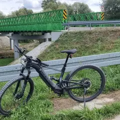 Rower elektryczny czeka na przygodę na trasie w Kazimierzu Dolnym. Zielony most w tle zaprasza do odkrywania malowniczych zakątków.