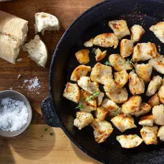 Krutonger i ugn, gyllene och krispiga, redo att förhöja vilken sallad som helst. En bit baguette och en skål flingsalt ligger bredvid.