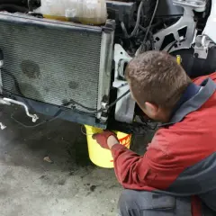Mechanik w rękawiczkach nalewa płyn do chłodnicy, pokazując, jak działa uszczelniacz do chłodnic.