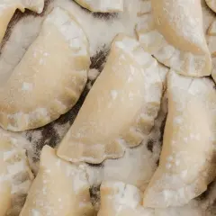 Surowe pierogi posypane mąką, gotowe do blanszowania.