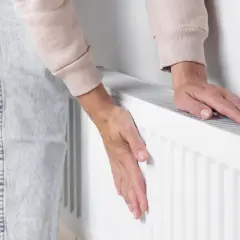 Dłonie sprawdzają temperaturę grzejnika. Jeden pion nie grzeje, co może oznaczać problem z ogrzewaniem.