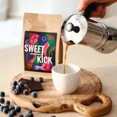 Kawa "Sweet Kick" z kawiarki nalewana do filiżanki. Na desce leżą jagody i czekolada. Idealna ilość kawy do kawiarki.