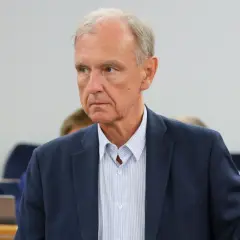 Portret starszego mężczyzny w granatowej marynarce i pasiastym jasnym koszuli.