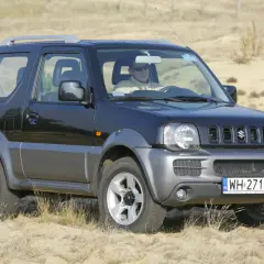 Czarny Suzuki Jimny na piasku. Kierowca w okularach. Pojemność baku tego modelu jest idealna na długie wyprawy.