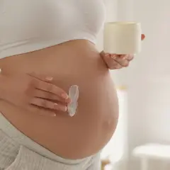 Kobieta w ciąży smaruje brzuch kremem. Delikatna pielęgnacja skóry, jak aloes w ciąży, to ważny element dbania o siebie.