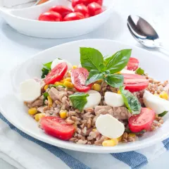 Deliziosa insalata di orzo con tonno, pomodorini, mais e mozzarelline, guarnita con basilico fresco. Un piatto completo e colorato.
