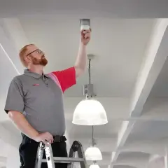 Techniker auf Leiter tauscht Melder, DIN 14675 konform.