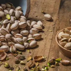 Pistacchi in una ciotola e sparsi su un tavolo di legno. Scopri le incredibili pistacchi proprietà per la tua salute.