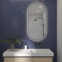 Eleganckie lustro z podświetleniem do łazienki nad kamiennym blatem z umywalką i roślinami.