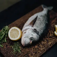 Un beau daurade prêt à être grillé, accompagné de citron frais et de romarin sur une planche en bois.