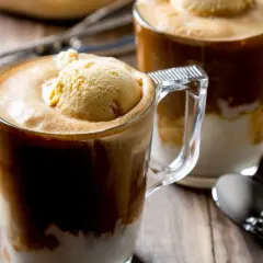 Dwa kubki caffe freddo z gałką lodów waniliowych na wierzchu, na drewnianym stole, obok ziaren kawy.