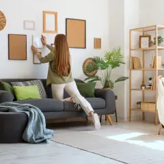 Kobieta wiesza obrazki w salonie. Idealne miejsce na wynajem mieszkania na miesiąc.