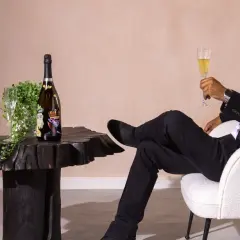 Mann in schwarzem Anzug genießt ein Glas Sekt neben einer Flasche, die wie der teuerster Sekt der Welt aussieht.