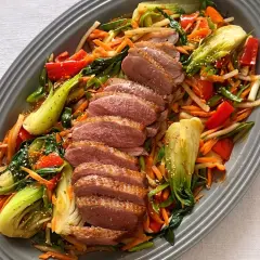 Skivad confiterad anka serveras med en färgstark wok av grönsaker som pak choi, morötter och paprika, toppad med sesamfrön.