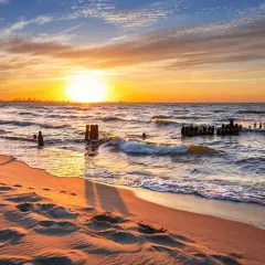 Zachód słońca nad Bałtykiem. Piasek na plaży, fale rozbijające się o pozostałości falochronów. Piękne wybrzeże polski.