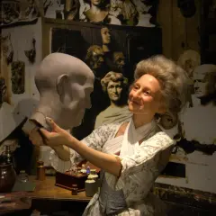 W muzeum figur woskowych artystka w historycznym stroju pracuje nad popiersiem.