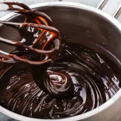 Ein Schneebesen rührt glänzende, dunkle schoko ganache in einem Topf.