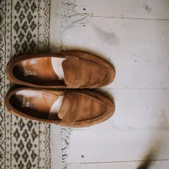Une paire de mocassins en daim marron, posée sur un tapis à motifs et un parquet. Idéal pour raviver la couleur du daim naturellement.