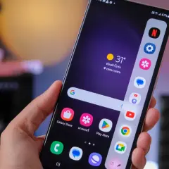 Dłoń trzyma smartfon Samsung S20 FE. Ekran pokazuje ikonki aplikacji i pogodę. Bateria szybko się rozładowuje, co widać po wskaźniku 67%.