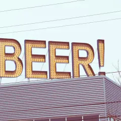 Grand panneau lumineux "BEER!" au-dessus d'un bâtiment moderne. Le nom de bière est écrit en lettres majuscules, illuminées par des ampoules.