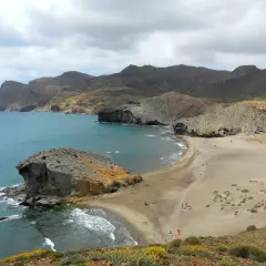 Paisaje de las mejores calas de Cabo de Gata, con formaciones rocosas, arena dorada y mar turquesa bajo un cielo nublado.