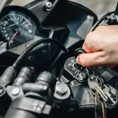 Mano girando la llave de contacto de una moto que se paró en marcha y no arranca. El tablero muestra el velocímetro.