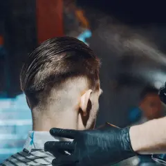Fryzjer spryskuje włosy klienta, tworząc modną undercut fryzurę.