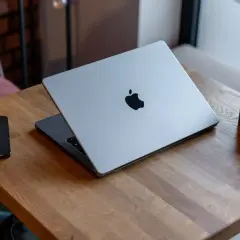 Srebrny MacBook z logo Apple, obok iPhone i aparat. Potężny procesor arm64 zapewnia płynność pracy.
